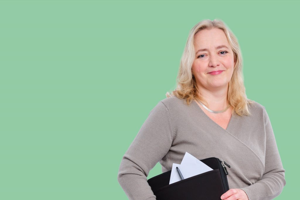 Milieuadviseur Ingrid met haar laptoptas in haar hand voor een groene achtergrond