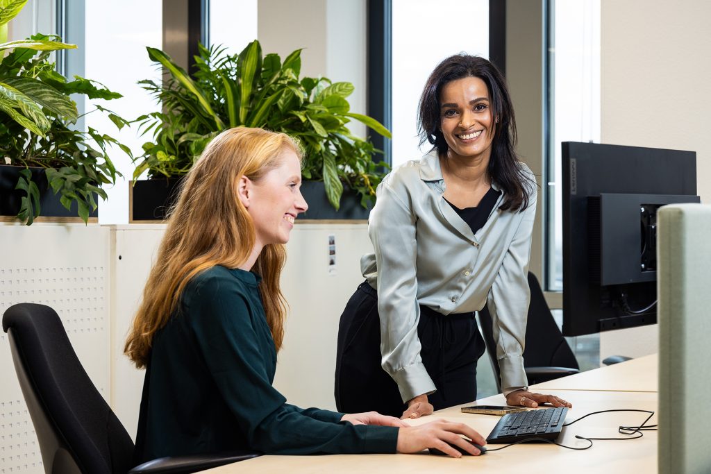 dame achter computer en dame staand bij haar collega